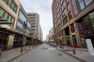 Wide city walkway between tall glass buildings on either side, with a yield-to-pedestrians sign in the distance.