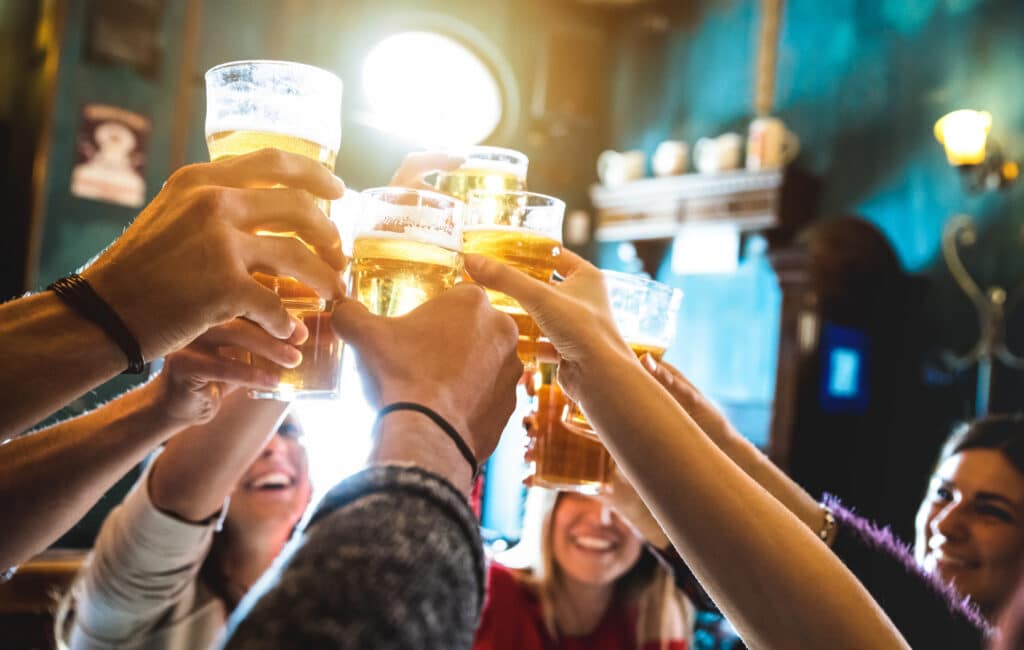 Group of friends raising beer glasses in a toast at a bar as they cheer together