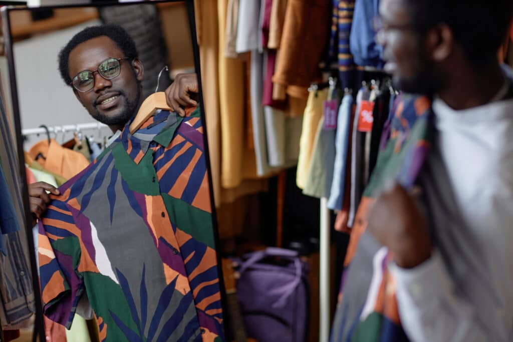 Man wearing a colorful abstract-pattern shirt looks at his reflection in a clothing-store mirror.