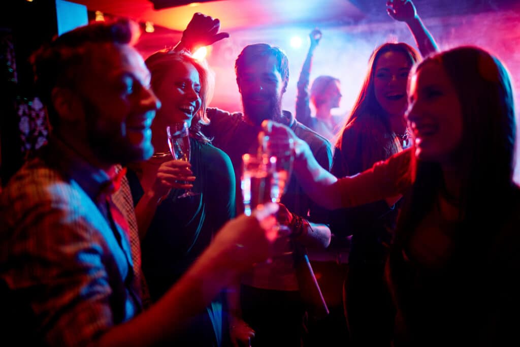 Group of friends toasting with drinks in a vibrant, neon-lit club.